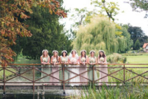 Bride and bridesmaids on a bridge over a river, willow tree in background