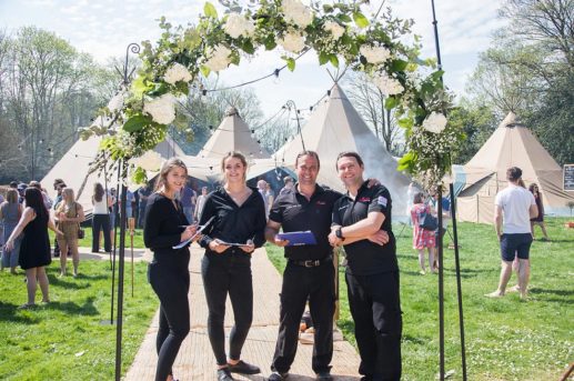Nyama team under floral arch with tipis in the background