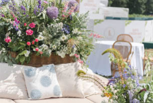Pink Purple floral display behind a wicker sofa with cushions outdoor hospitality area