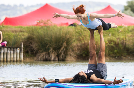 couple going yoga pose on paddle board on lake with red stretch tent in background