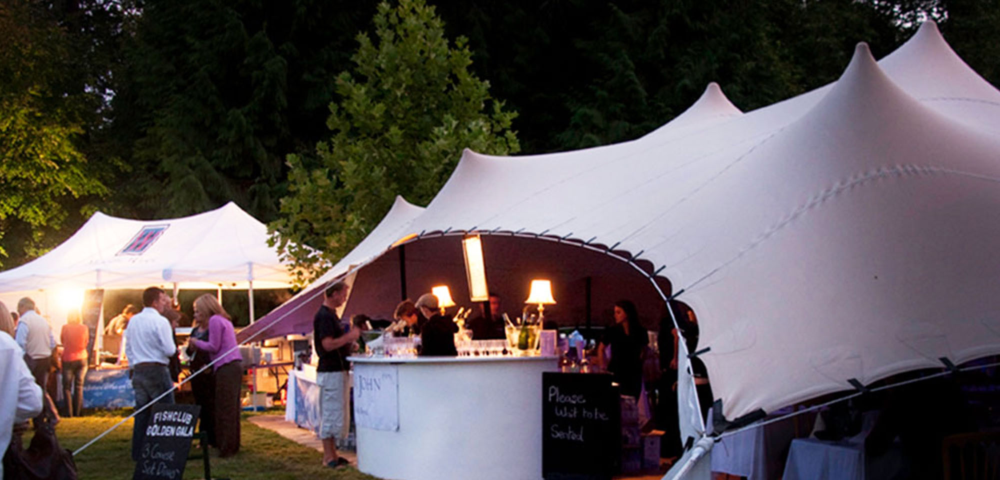 Beige Strech tent, pop up restaurant, lit up, dusk.