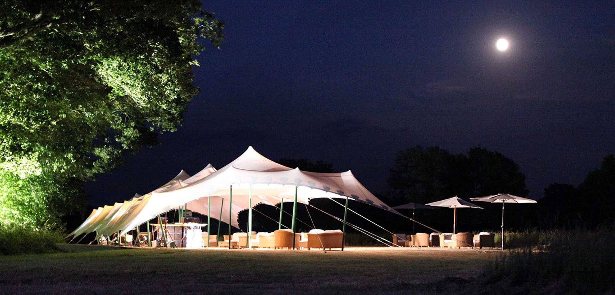 White stretch tent by moonlight, up lit trees.